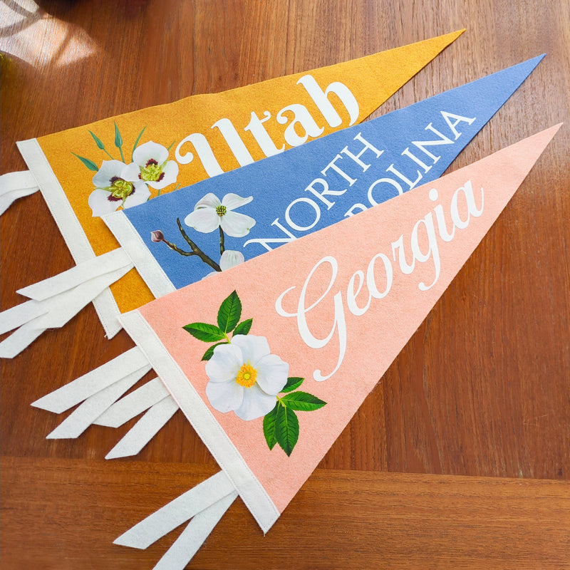 A photo of three pennants that are printed with "Georgia", "North Carolina" and "Utah" along with their state flowers