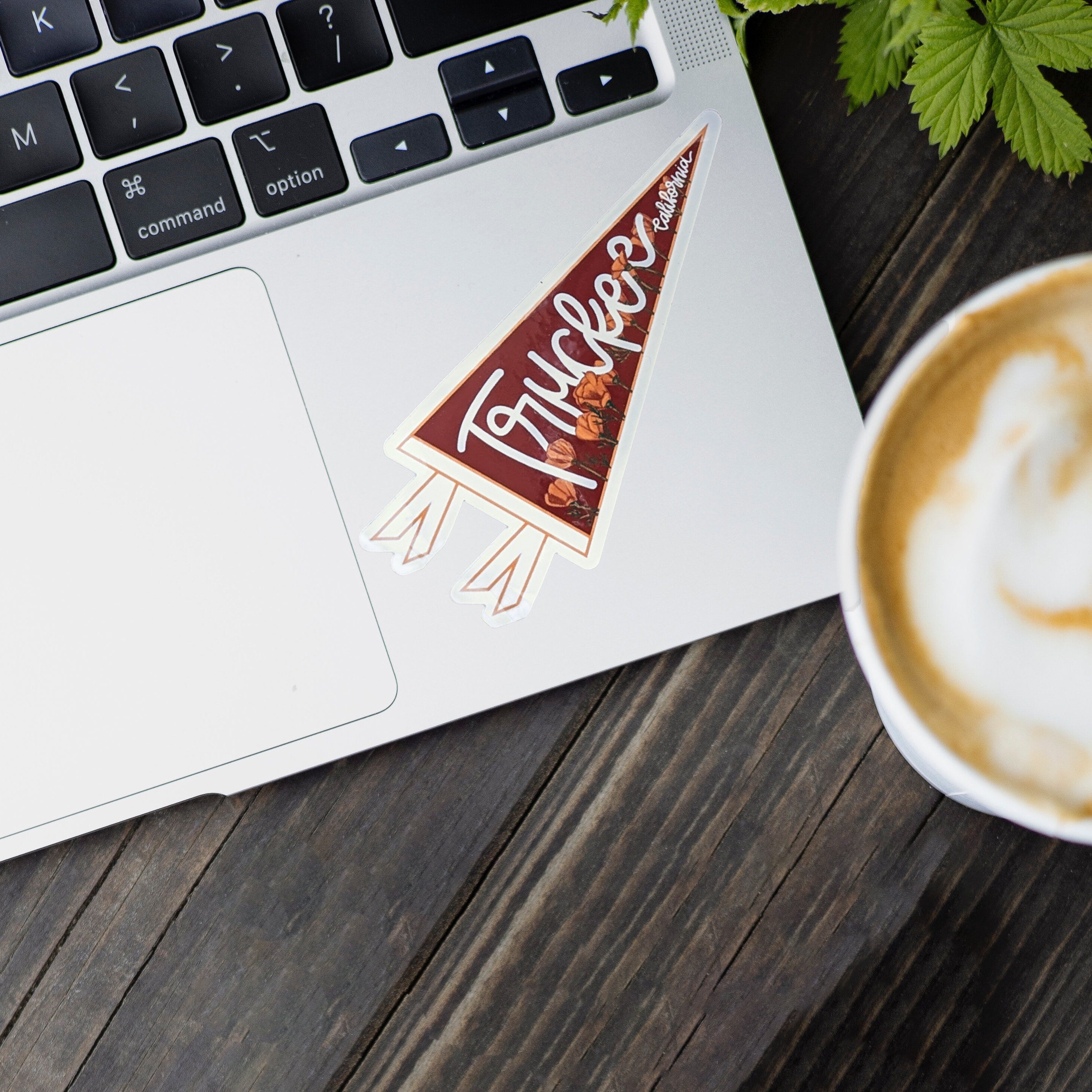 Laptop with a pennant-shaped "Truckee, California" sticker on a wooden surface next to a cup of coffee