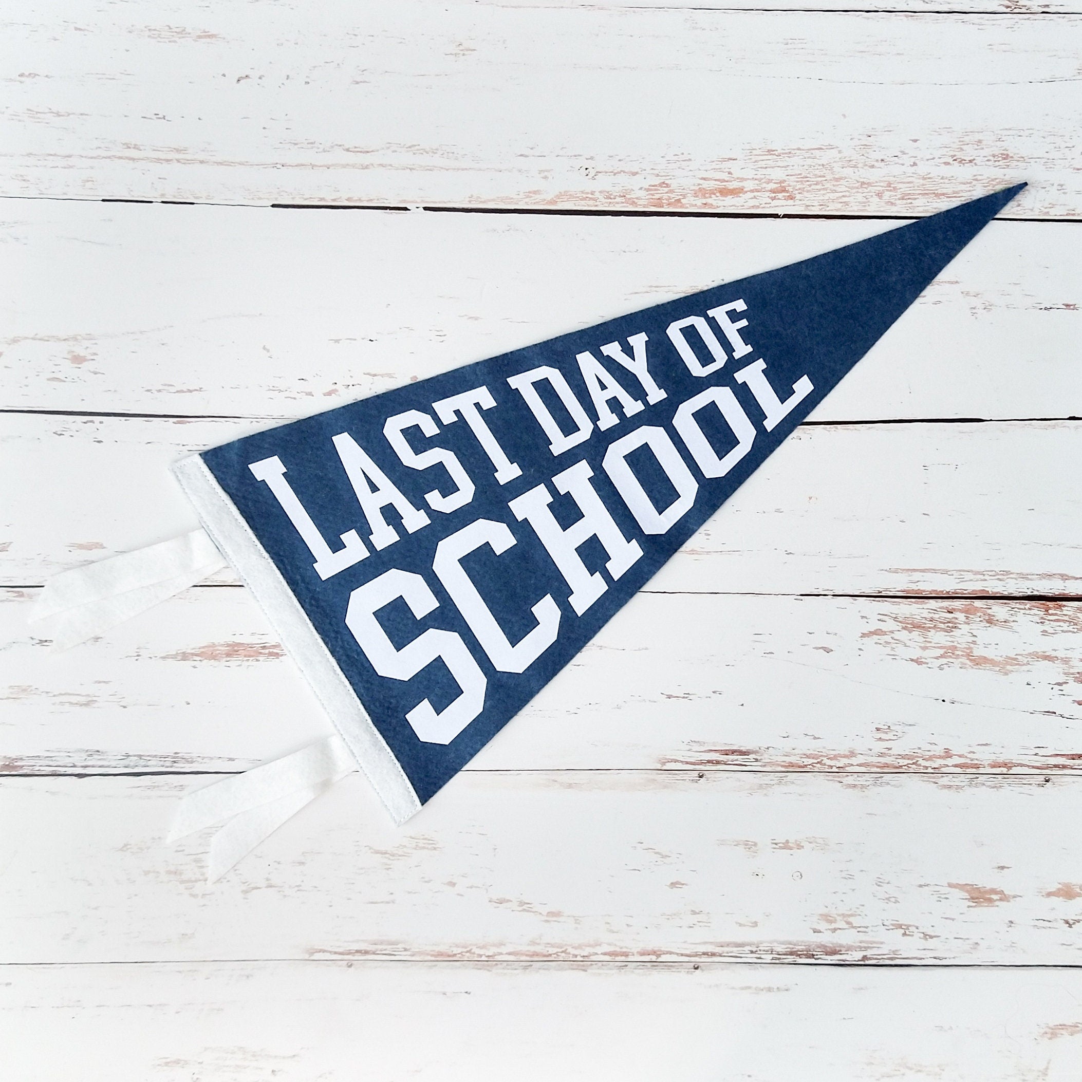 Navy blue and white pennant with 'Last Day of School' text on a wooden surface