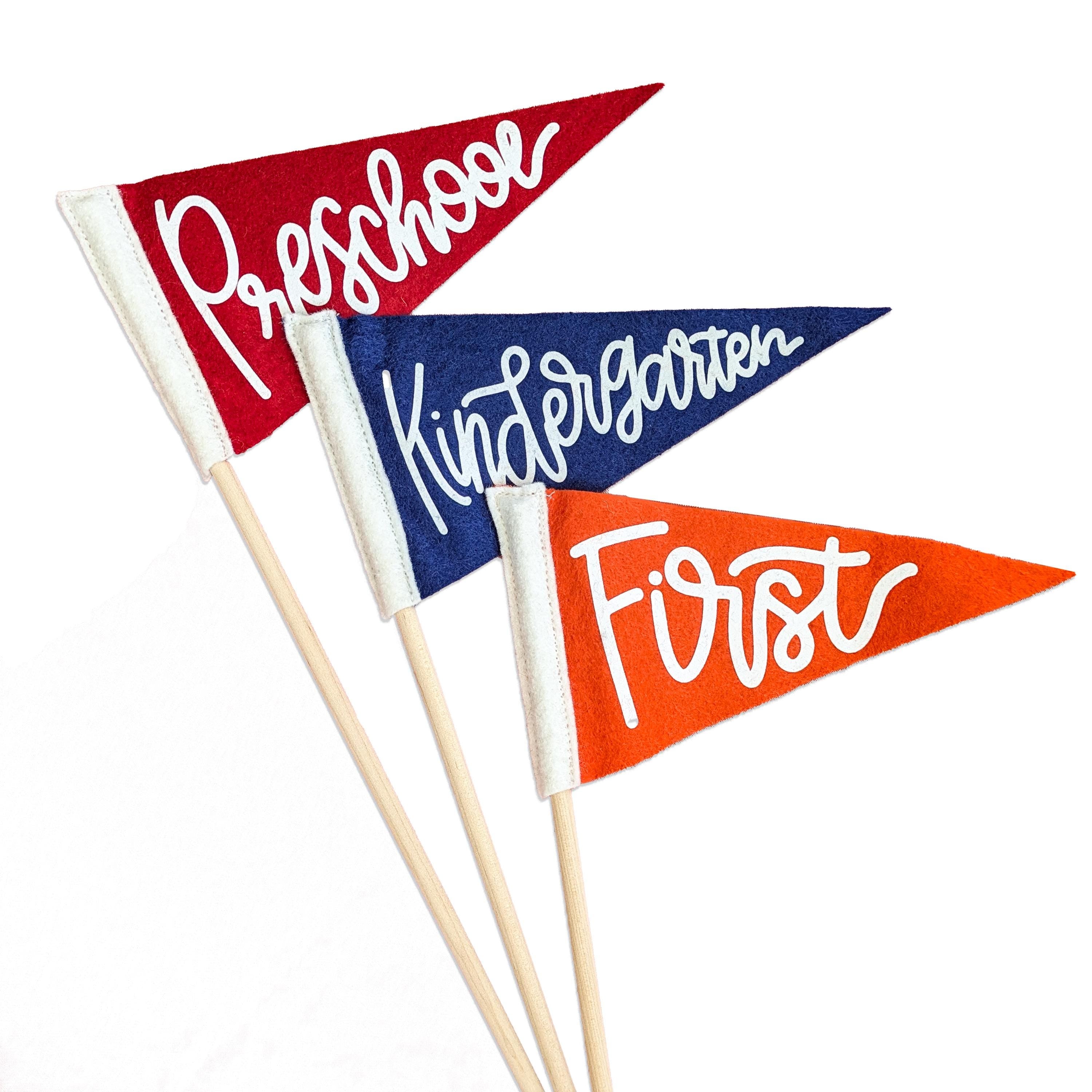 Three mini pennant flags that say 'Preschool', 'Kindergarten', and 'First' on a white background.