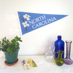 Decorative items including a potted plant, bottles, and a 'North Carolina' banner with flowers on a white surface.