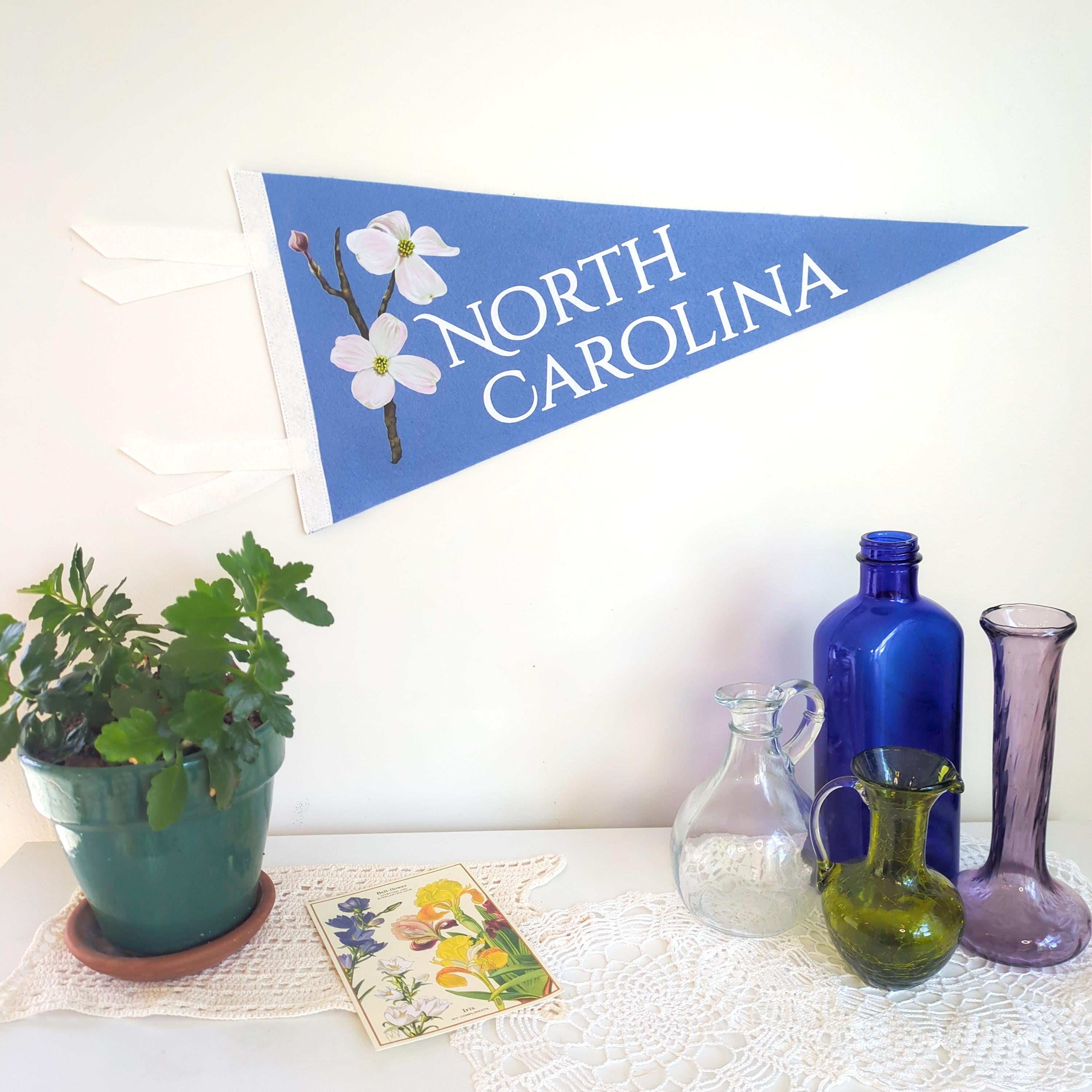 Decorative items including a potted plant, bottles, and a 'North Carolina' banner with flowers on a white surface.