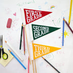Colorful pennant flags that say 'First Grade', 'Second Grade', and 'Third Grade' on a school-themed background with pencils and scissors.