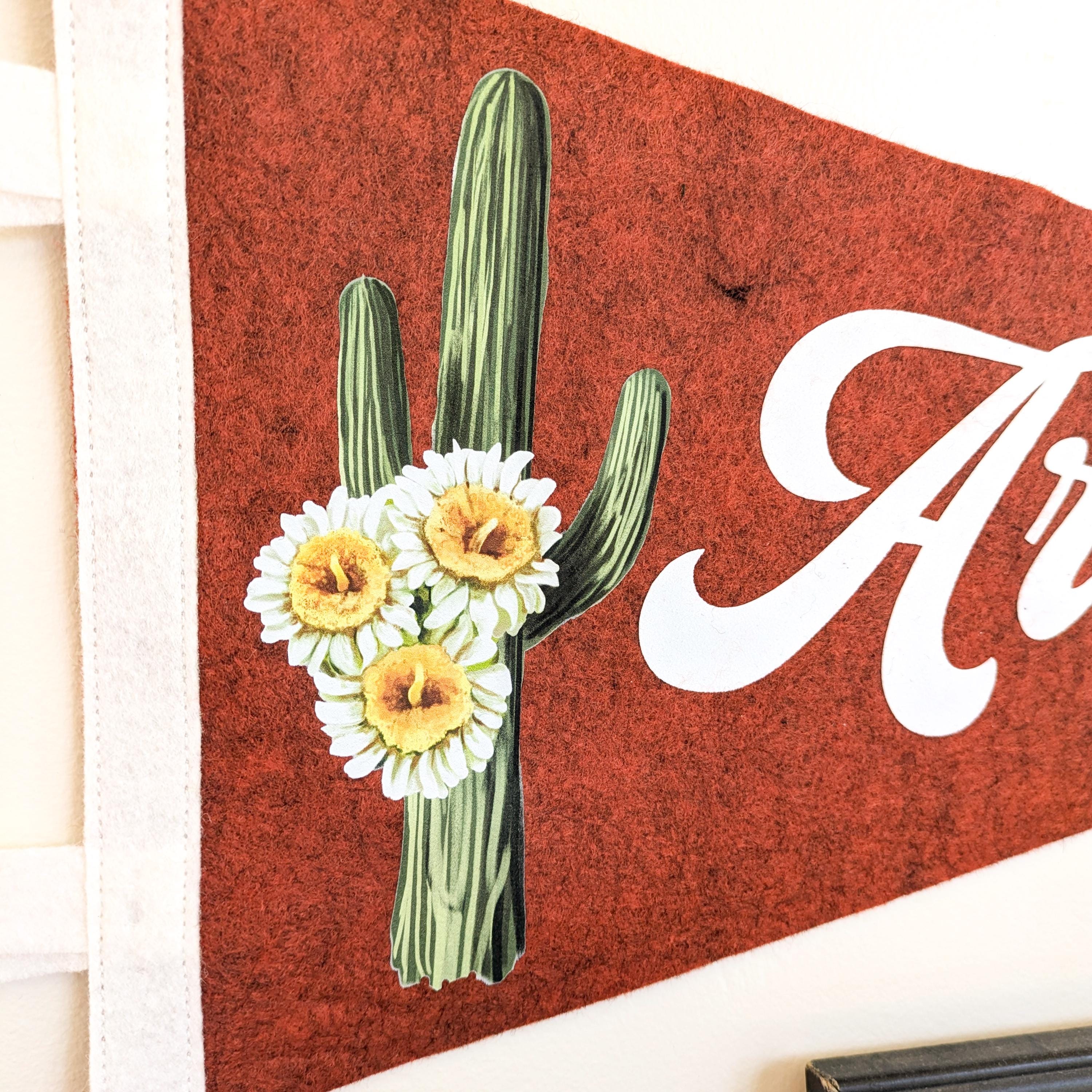 a reddish brown felt pennant with a cactus and flowers design and 'Arizona' text.