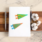 a noteboook with a colorful Pennant-shaped sticker that says "What if It All Works Out" , and a colorful pennant sticker that says "Tummyache Survivor"