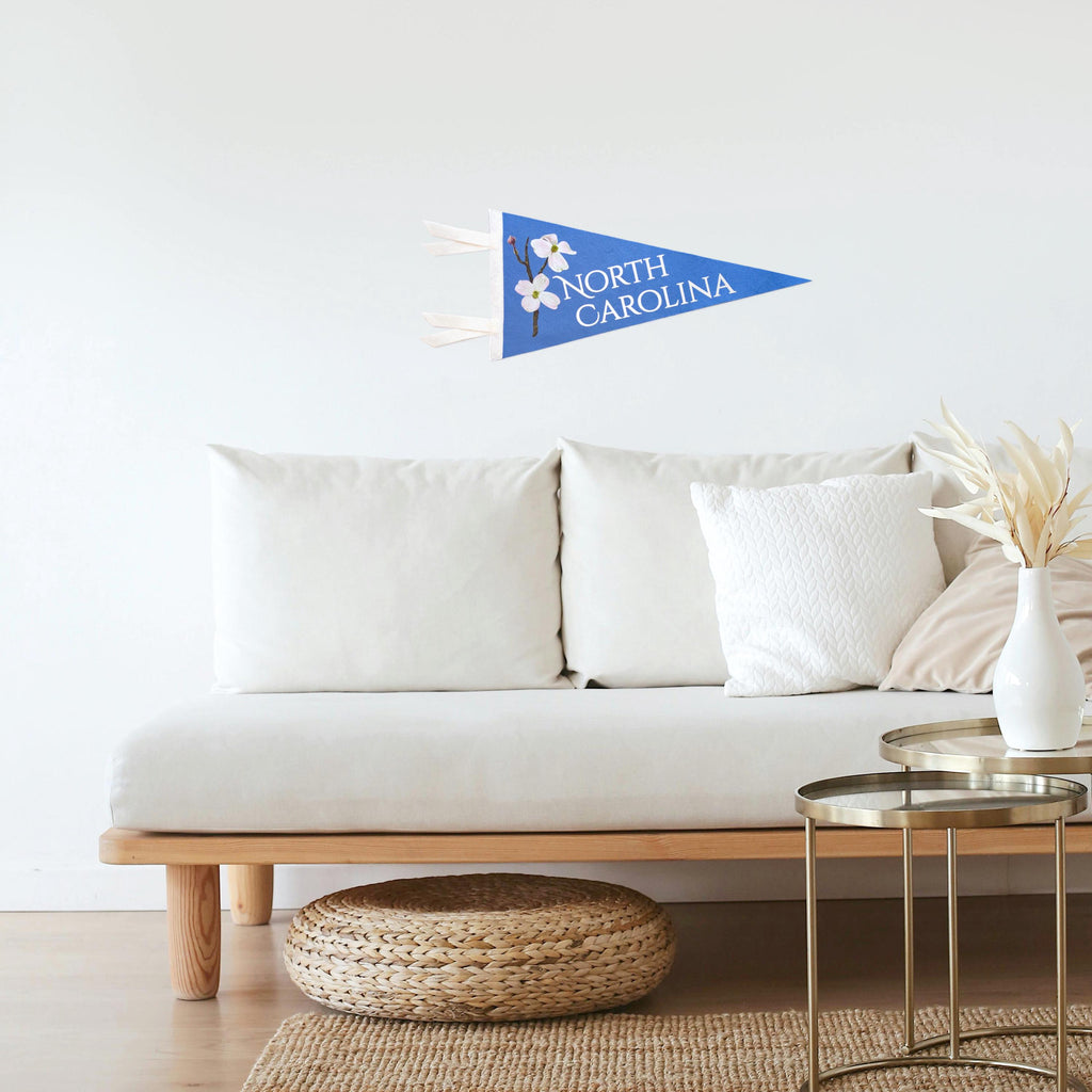 White sofa with decorative pillows in a living room setting, featuring a light blue 'North Carolina' pennant