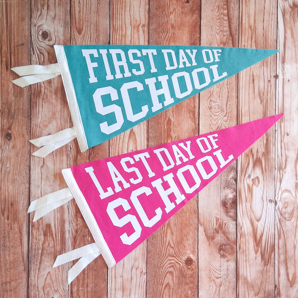 Two pennant flags, one blue and one pink, with 'First Day of School' and 'Last Day of School' text on a wooden background.