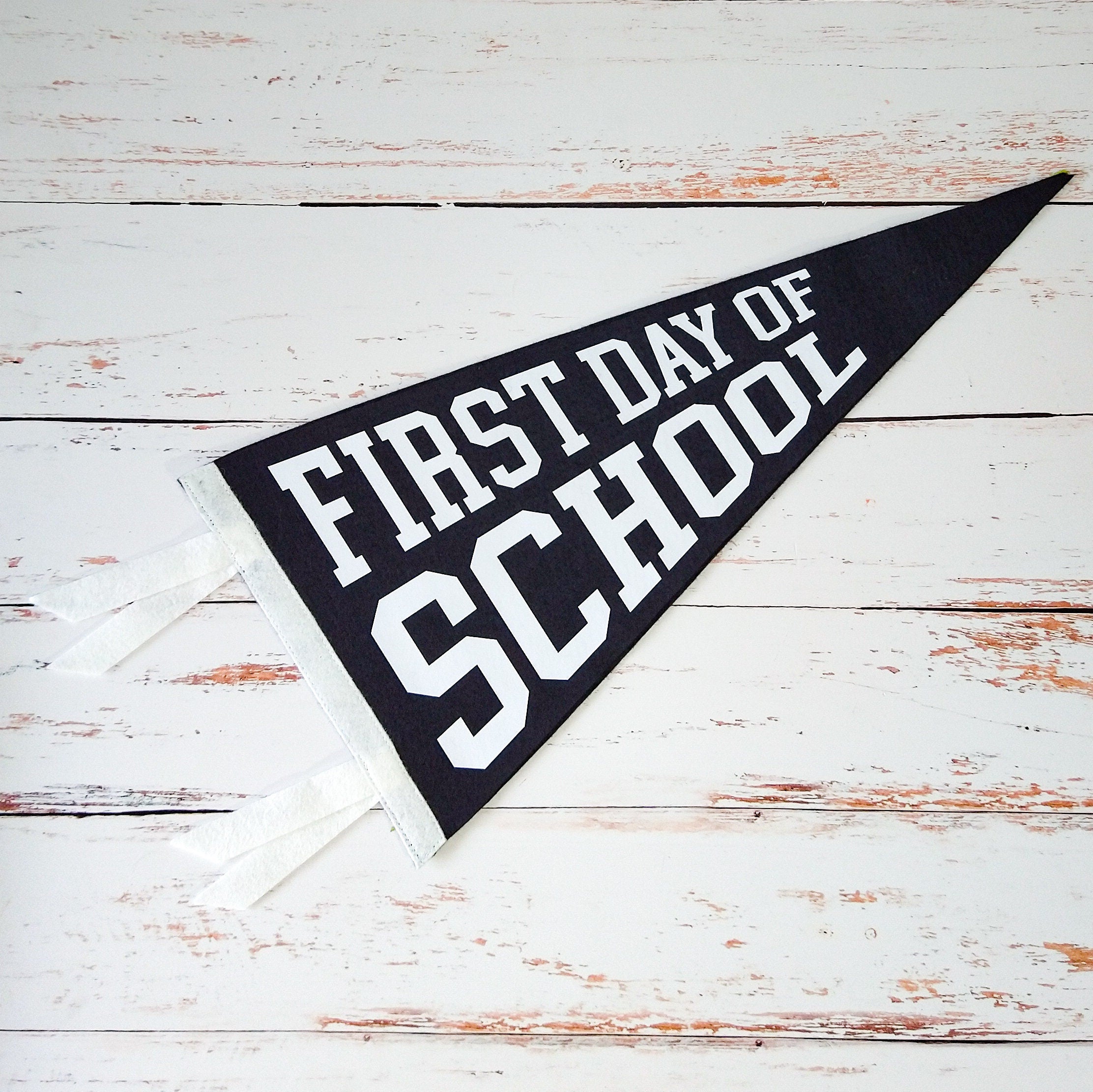 Black and white pennant with 'First Day of School' text on a wooden surface