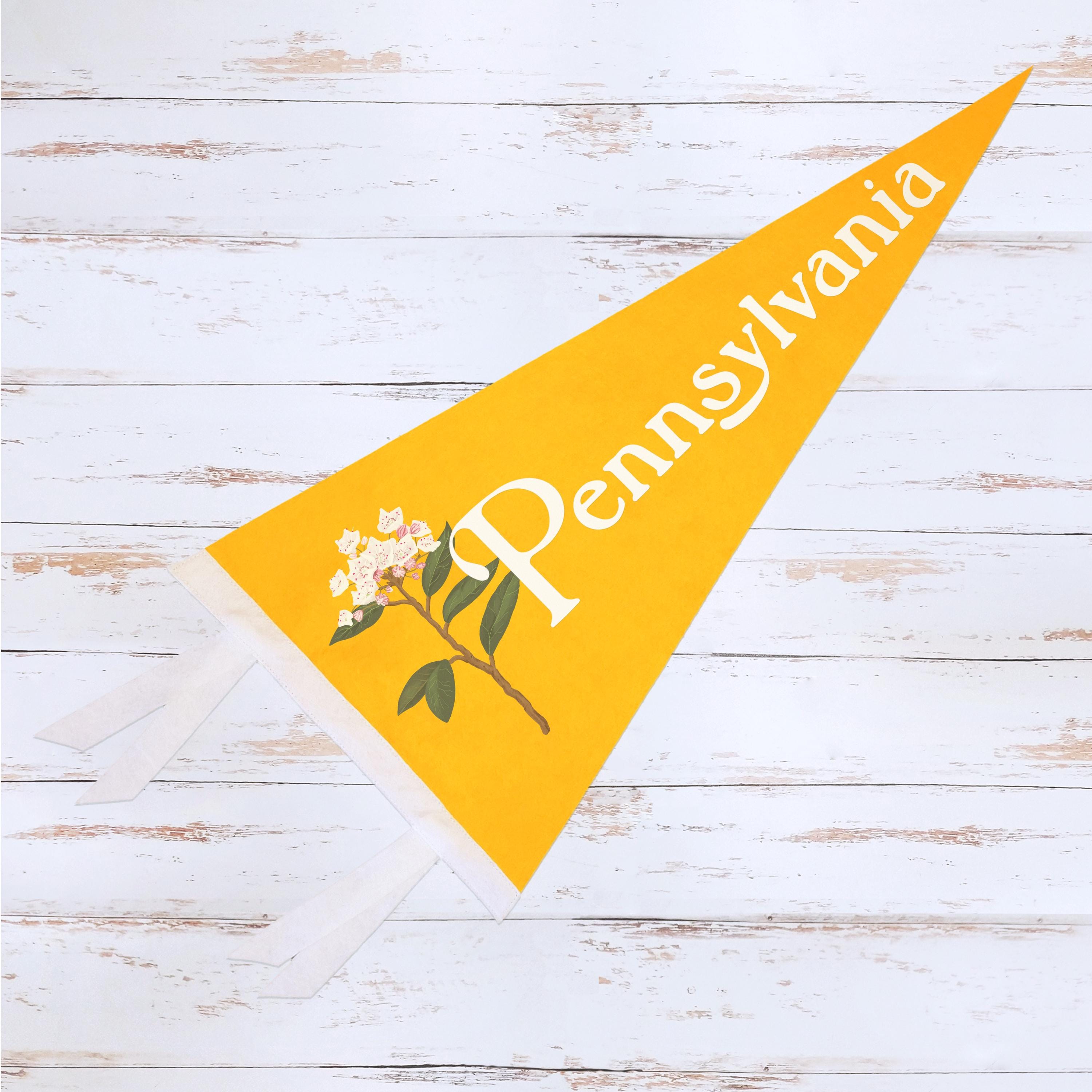 A yellow Pennsylvania-themed decorative flag with floral design on a wooden surface