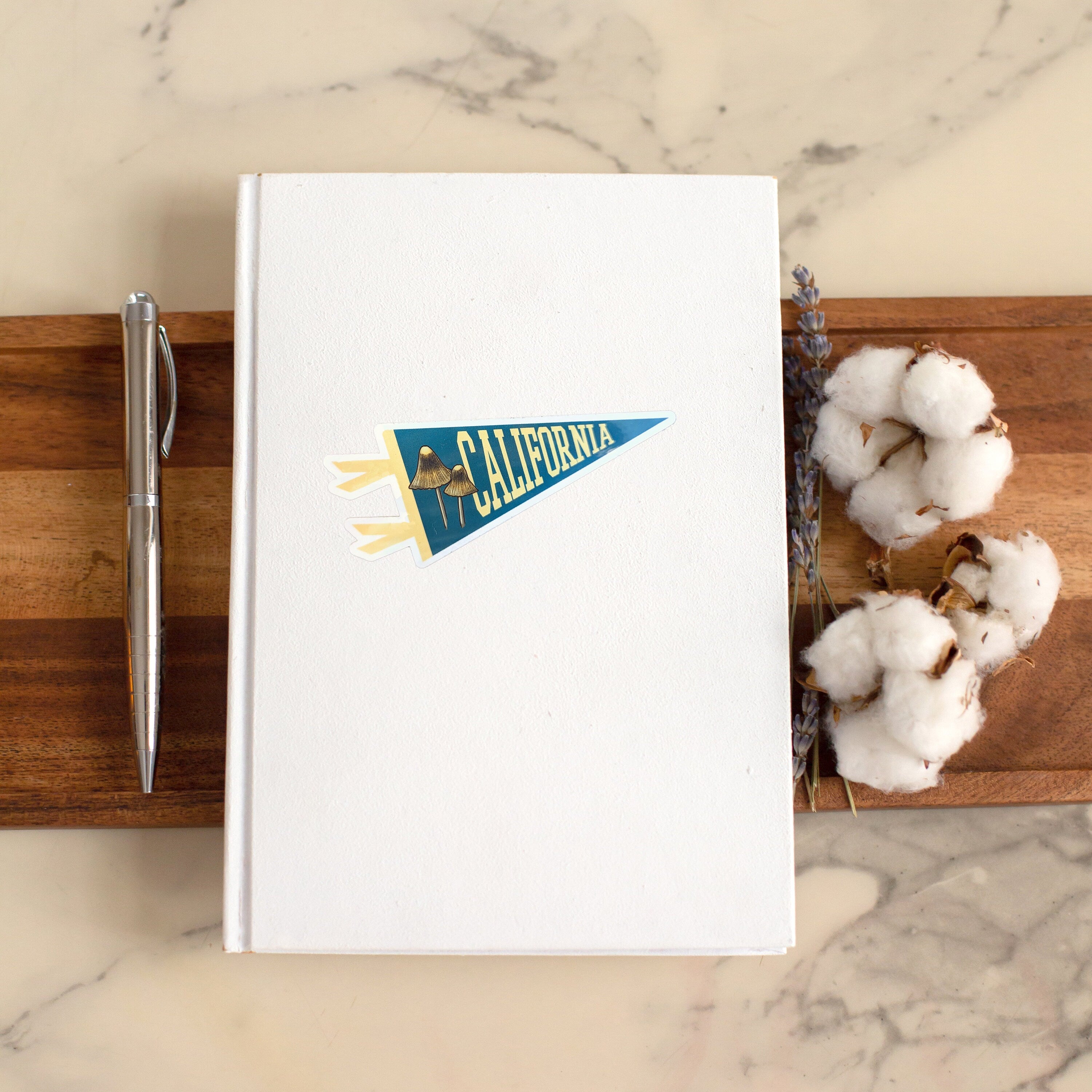 White notebook with a pennant-shaped blue and yellow sticker with 'California' text and a mushroom illustration
