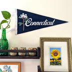 Navy blue 'Connecticut' pennant with floral design on a wall above a shelf with decorative items.