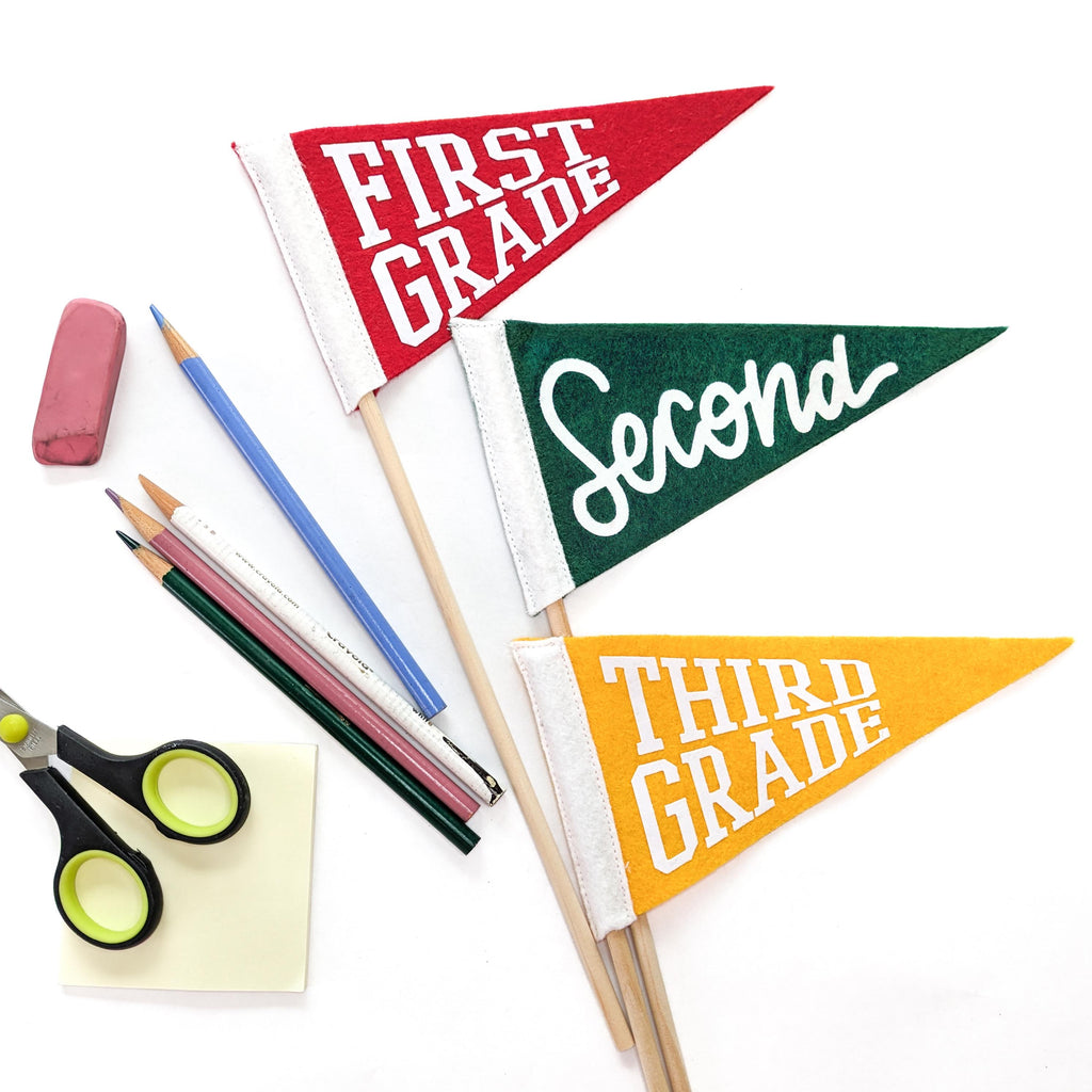 Three colorful pennant flags labeled 'First Grade', 'Second', and 'Third Grade' with school supplies on a white background.