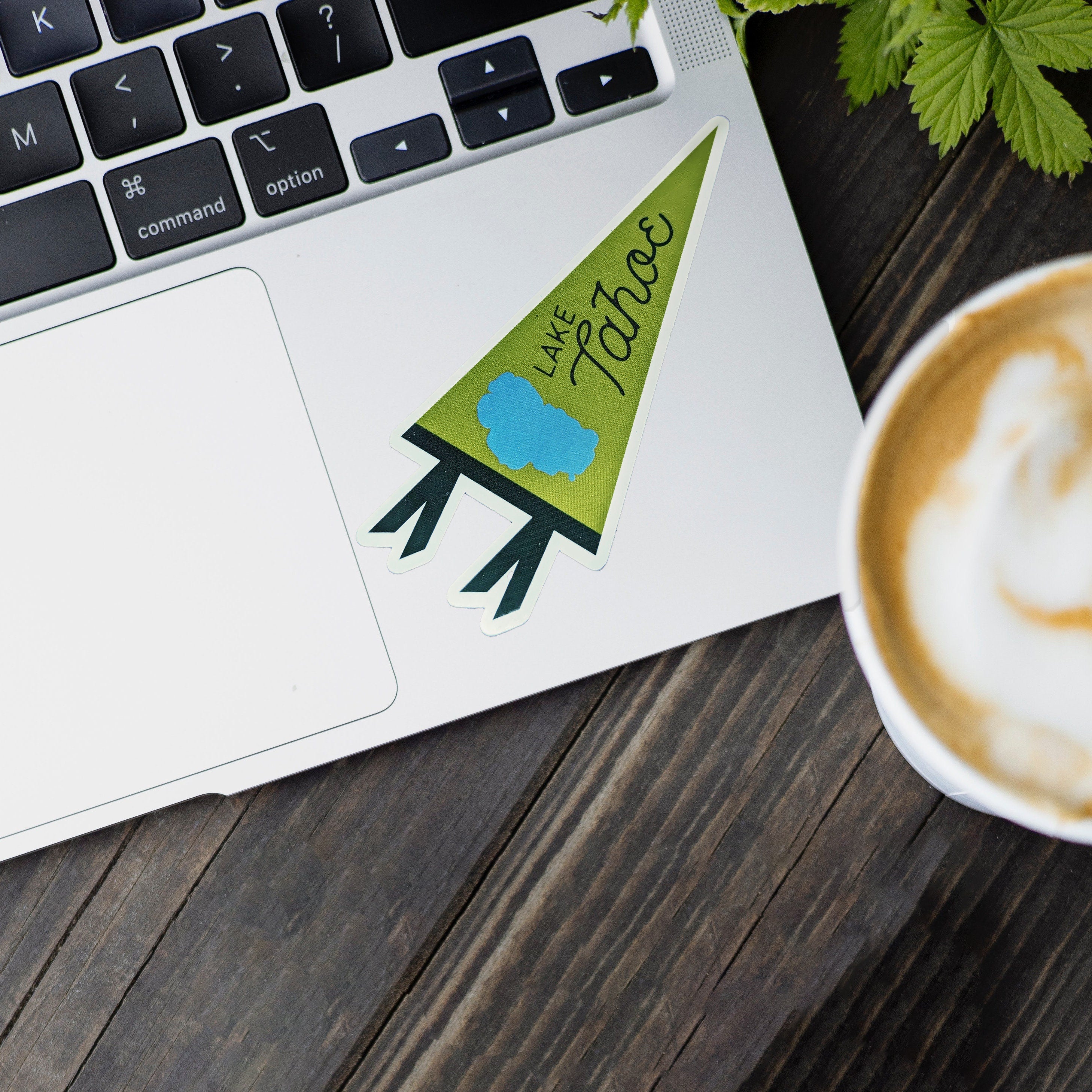 Laptop with a 'Lake Tahoe' sticker on a wooden surface next to a cup of coffee.