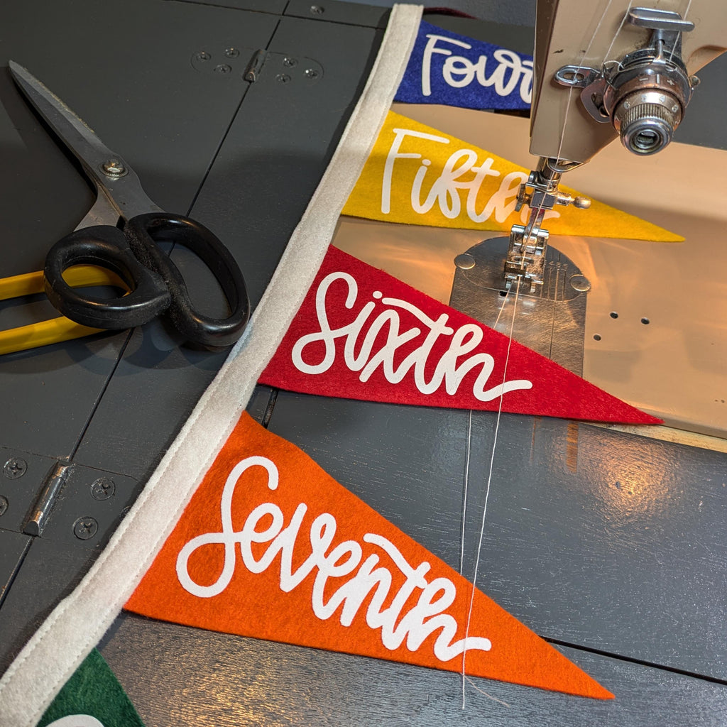 Pennant flags with numbers and letters being sewn on a sewing machine, with scissors nearby.