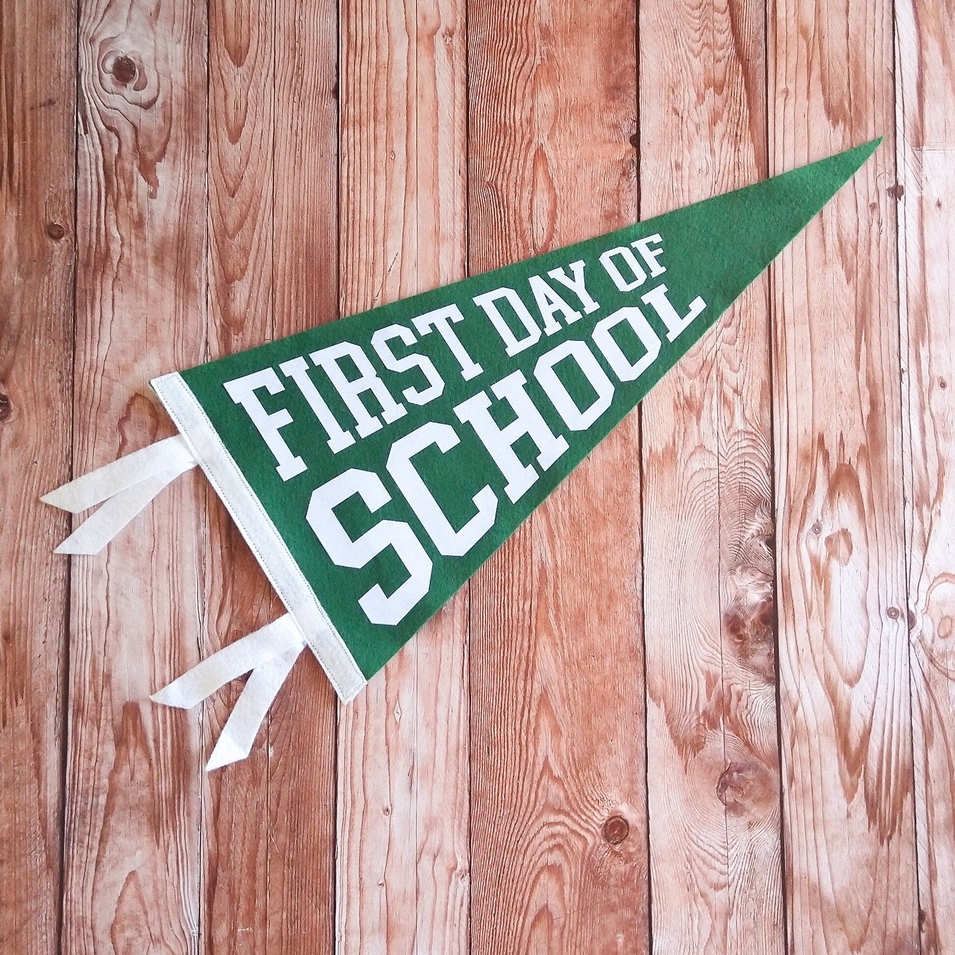 Green and white 'First Day of School' pennant on a wooden background