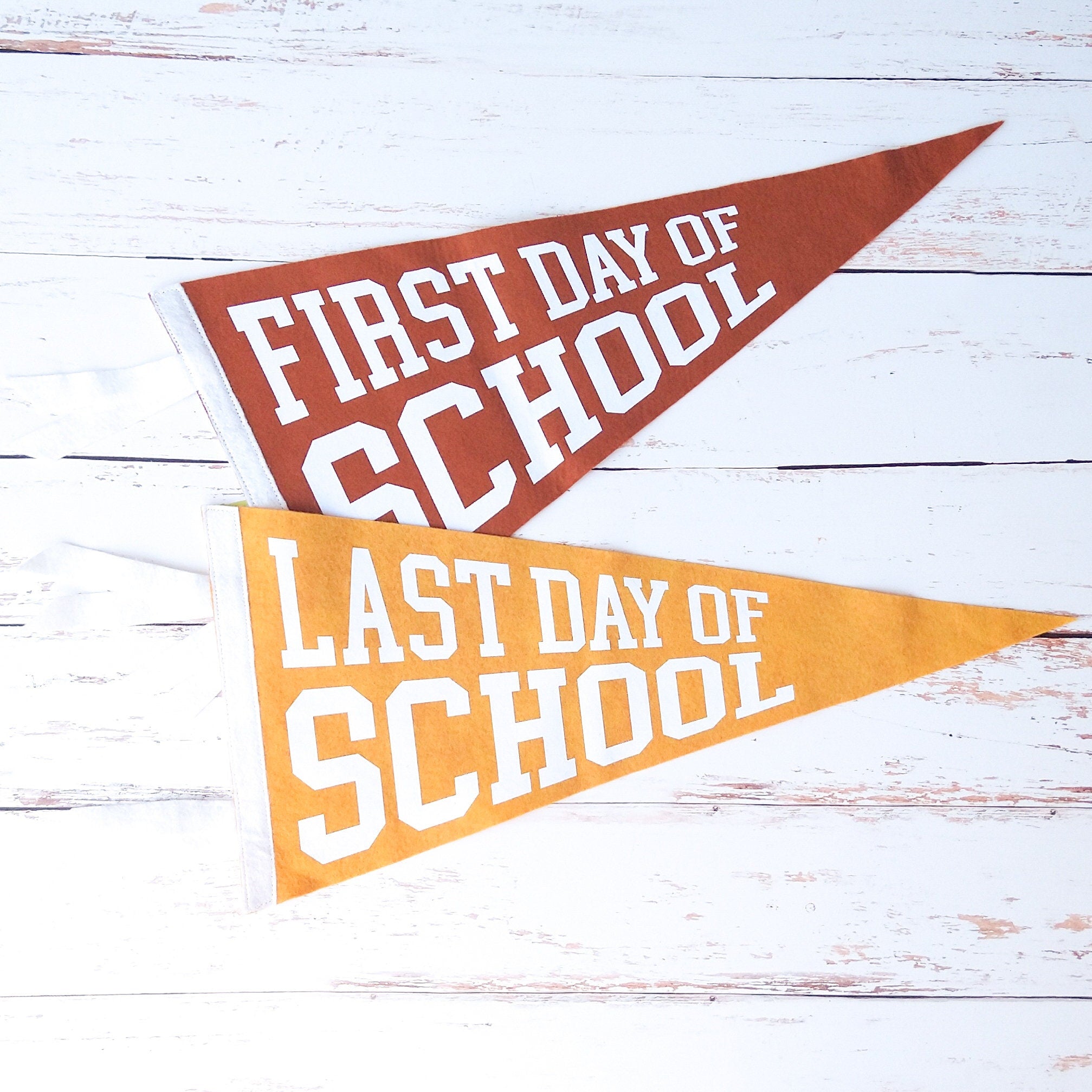 Two pennant flags with 'First Day of School' and 'Last Day of School' text on a wooden surface.