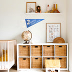 Nursery with a white dresser, wicker baskets, a crib, and a blue North Carolina pennant on the wall.
