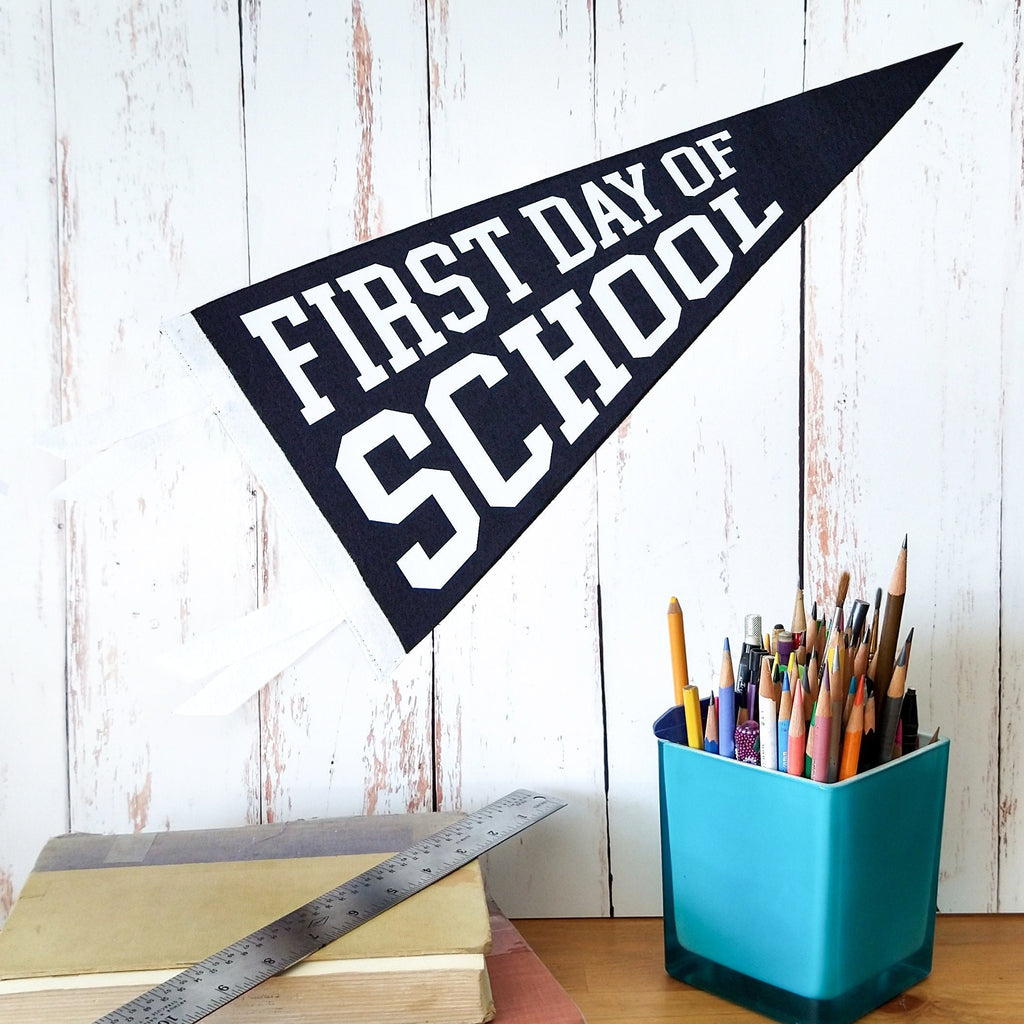 Pennant with 'First Day of School' text next to a blue pencil holder on a wooden surface.