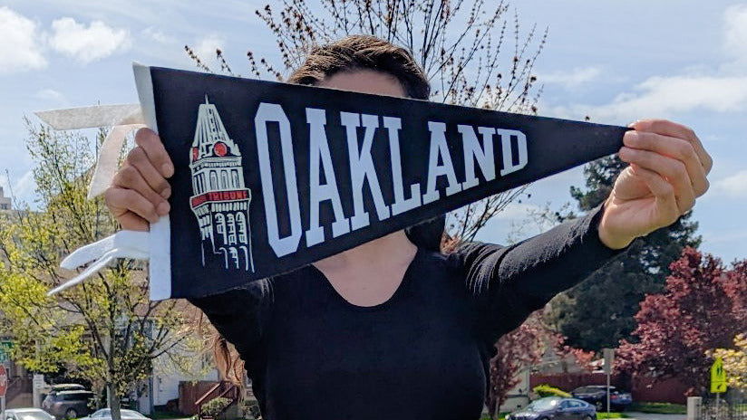 Person holding a 'Oakland' pennant with a tribune tower graphic against a suburban backdrop